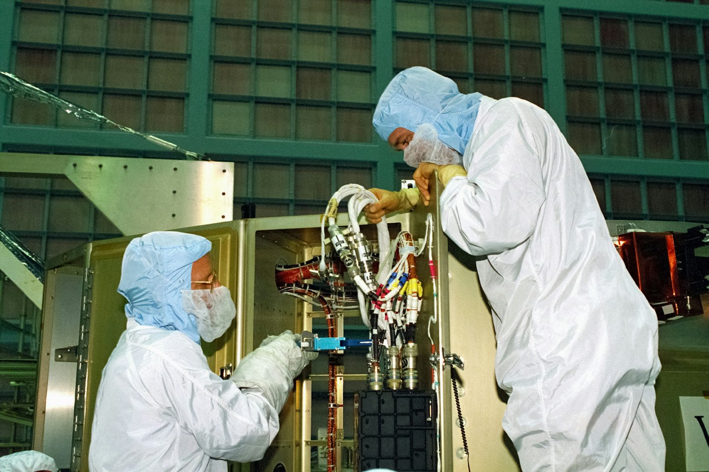 Dwóch techników w kombinezonach cleanroom montuje skomplikowany sprzęt elektroniczny.